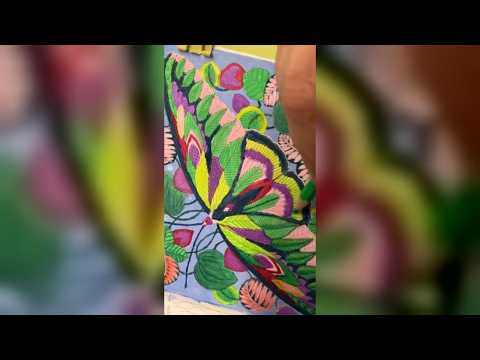 Butterfly with leaf-patterned wings in lime yellow, purple and pink among green and coral leaves in Millie Marotta's Curious Creatures, being colored with a green colored pencil