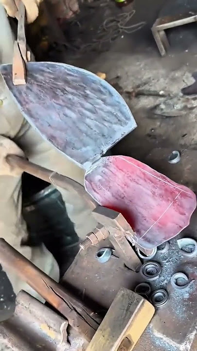 A worker firmly holds the heated metal piece with tongs shaping its curved edge carefully on