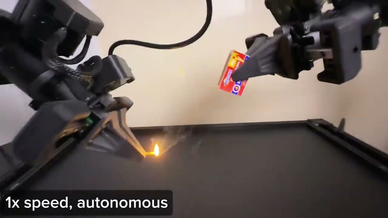 Two black Trossen robot arms working together over a table, one holding a red matchbox while the other strikes a match.