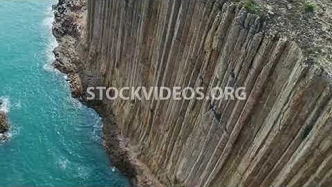 steep cliff on an island, igneous volcanic rock, basalt columns of hexagonal shape, sea view
