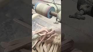 smoothing wooden clothes hangers using a rotating drum sander machine to ensure a clean surface
