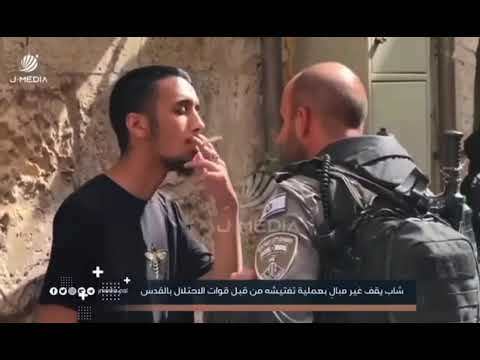 شاب فلسطيني يقف غير مبال بعمليه تفتيشه من قبل قوات الاحتلال