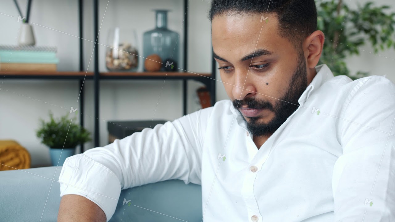 Serious African American man working with laptop computer on couch at home
