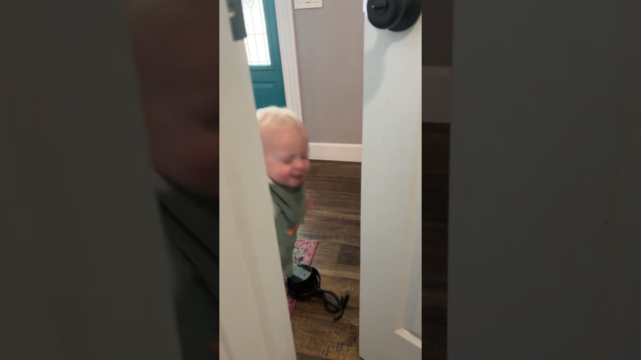 Little boy in green overalls trips and faceplants onto side of door
