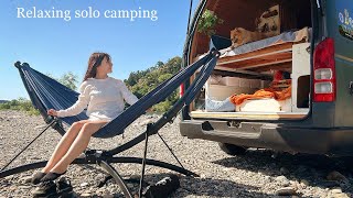 Relaxed solo camping on the riverbank. A woman grills meat while relaxing in a hammock.