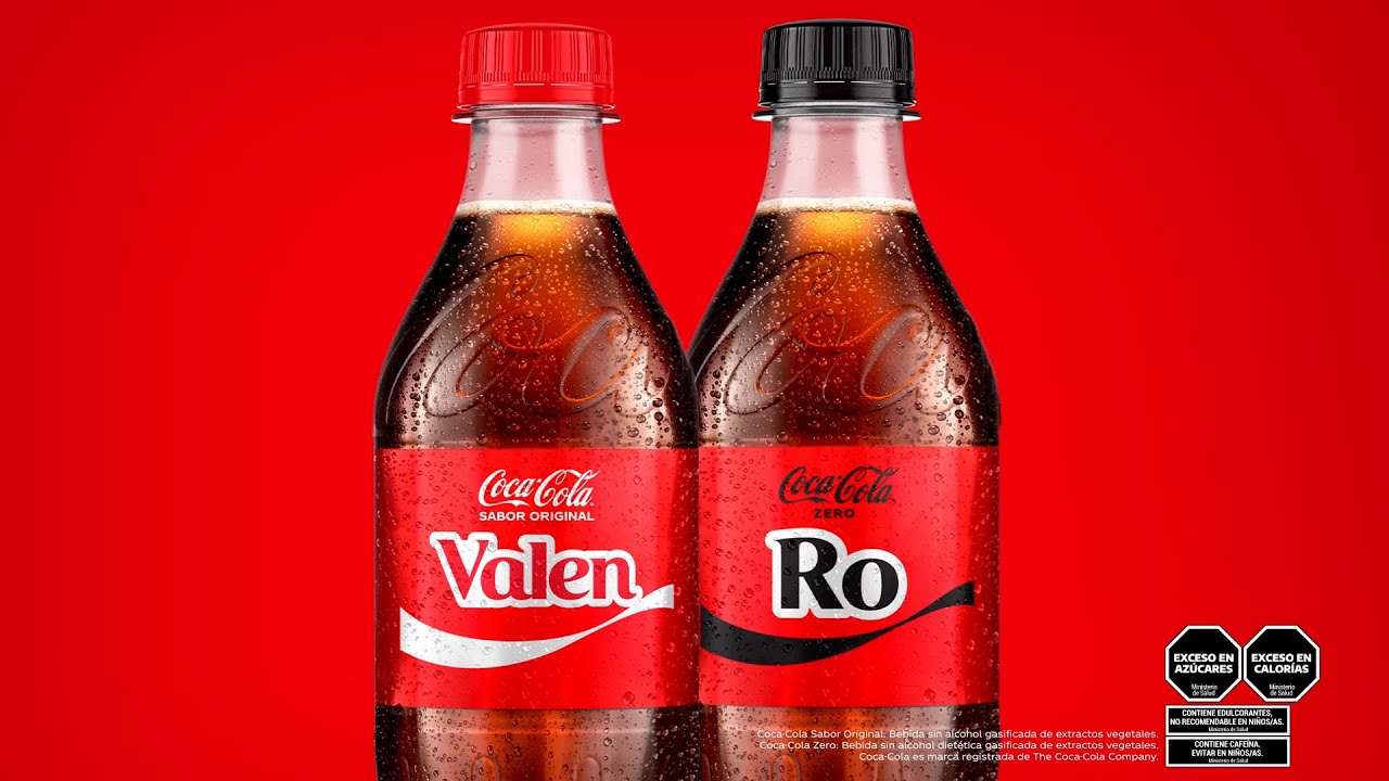 Dos botellas de Coca-Cola personalizadas con los nombres impresos en la etiqueta, fondo rojo intenso y gotas de condensación visibles.