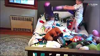 Boy uses inflated purple hammer to tap little brother on back while laying on bed (Security camera)