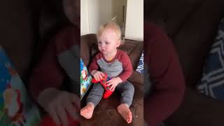 Woman throws cheese at baby seated on couch holding video game remote controller
