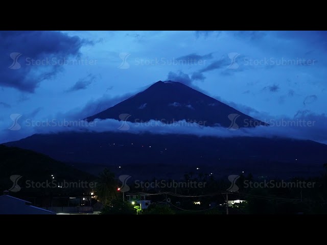 agung volcano mountain time lapse sunset getting dark clouds dancing city shining with lamps class=