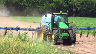 John Deer pulling tank with sprayer through corn field.