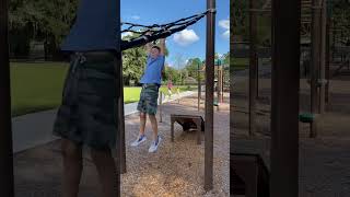 Boy jumps from ramp and hangs on black netting at playground then lands on wood chips on back