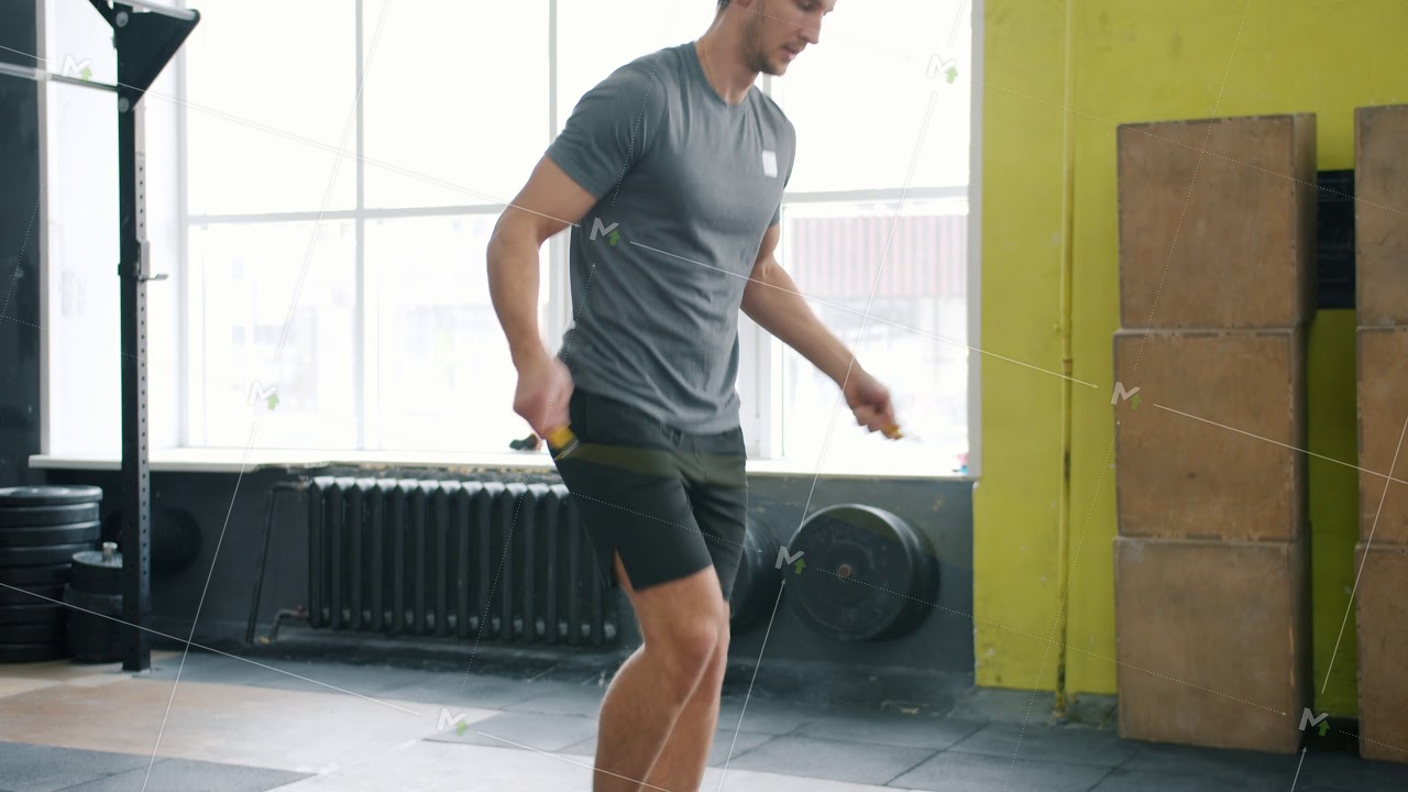 Tiltup slow motion of fit young man jumping with skipping rope indoors