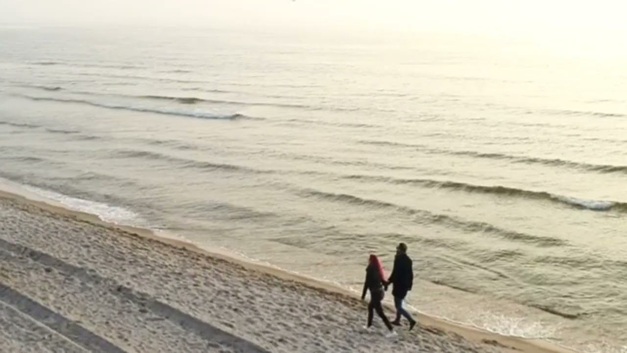 Young couple holding hands walking on beach at sunset