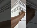 Craftsman installs crown molding into ceiling corner with compound