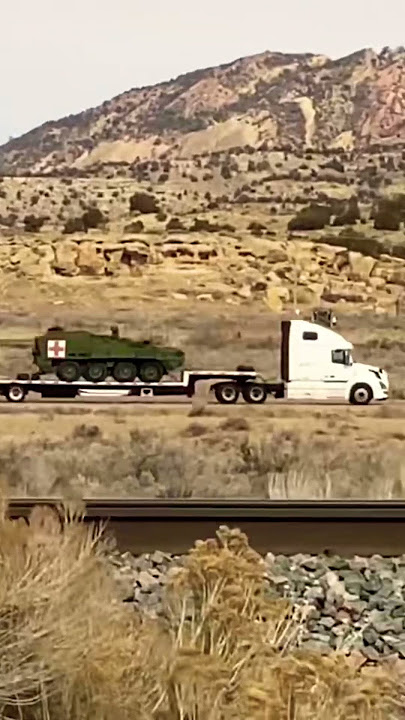 Dark Green Military Armored Vehicle being transported on back of Semi Trailer on the interstate