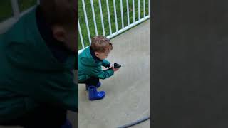 Boy sprays himself on his face with garden water hose