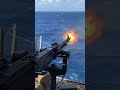 Naval machine gun mounted on ship deck firing rapid bullets, bright muzzle flash sparks.