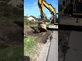 Екскаватор працює біля дороги та знімає шар землі з травою