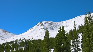4K Aerial parallax of a snowy rocky mountain peak with trees in the foreground