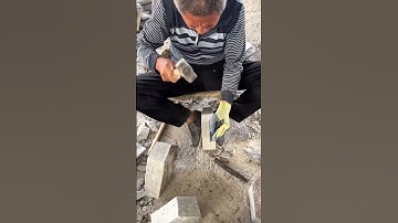Worker shapes rough stone block manually using hammer and chisel for construction work