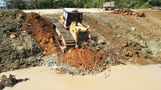 Expert operator KOMATSU D60E dozer pushing rock & dirt clearing pond, 15 ton trucks transport soil