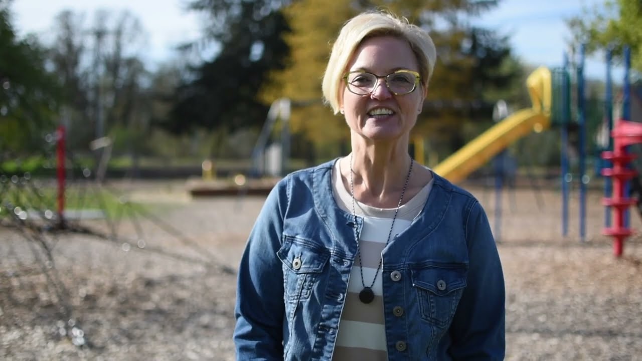 Video preview image of A woman stands smiling in front of a children's playground; click to visit the ParentSquare post with the video