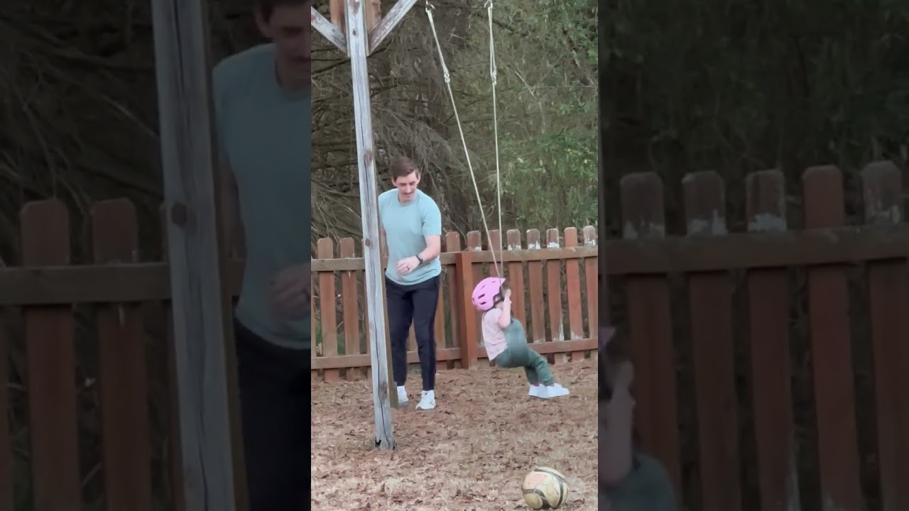 Guy pushes little girl in pink helmet on swings then leg hits wood post causing her to spin