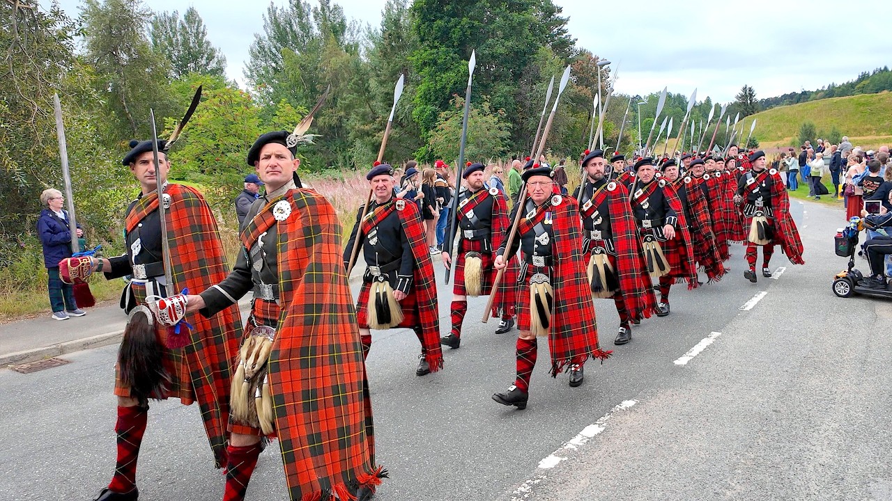 Lonach Highlanders salute memorial on march into Bellabeg during 2025 Lonach Gathering in Scotland