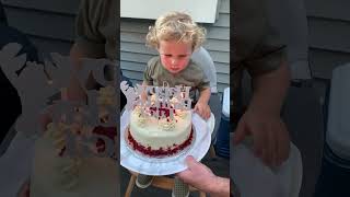 Little boy in highchair blows out birthday cake then uses his finger to touch flame on candle