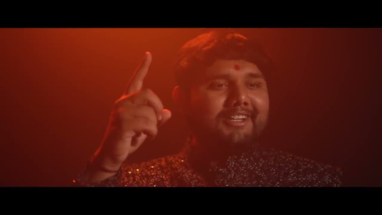 Uday Dhadhal pointing upward mid-song, lit in deep red — still from Meldi Vare Chade