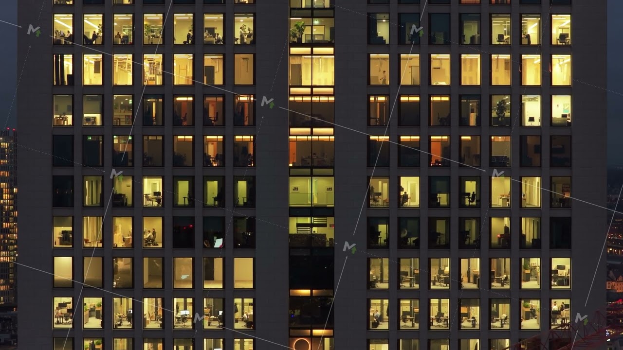 Aerial view of windows of modern office building at night. Lights on and people working late inside