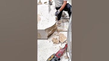 Worker carving large stone block using hammer and chisel