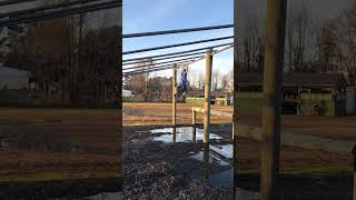 Boy hangs from wood panels and attempts to jumps on to log