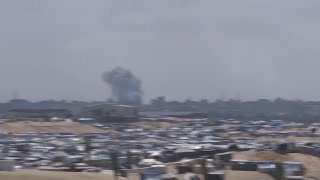 Displaced people at Israel-declared humanitarian zone, smoke plume rises in distance
