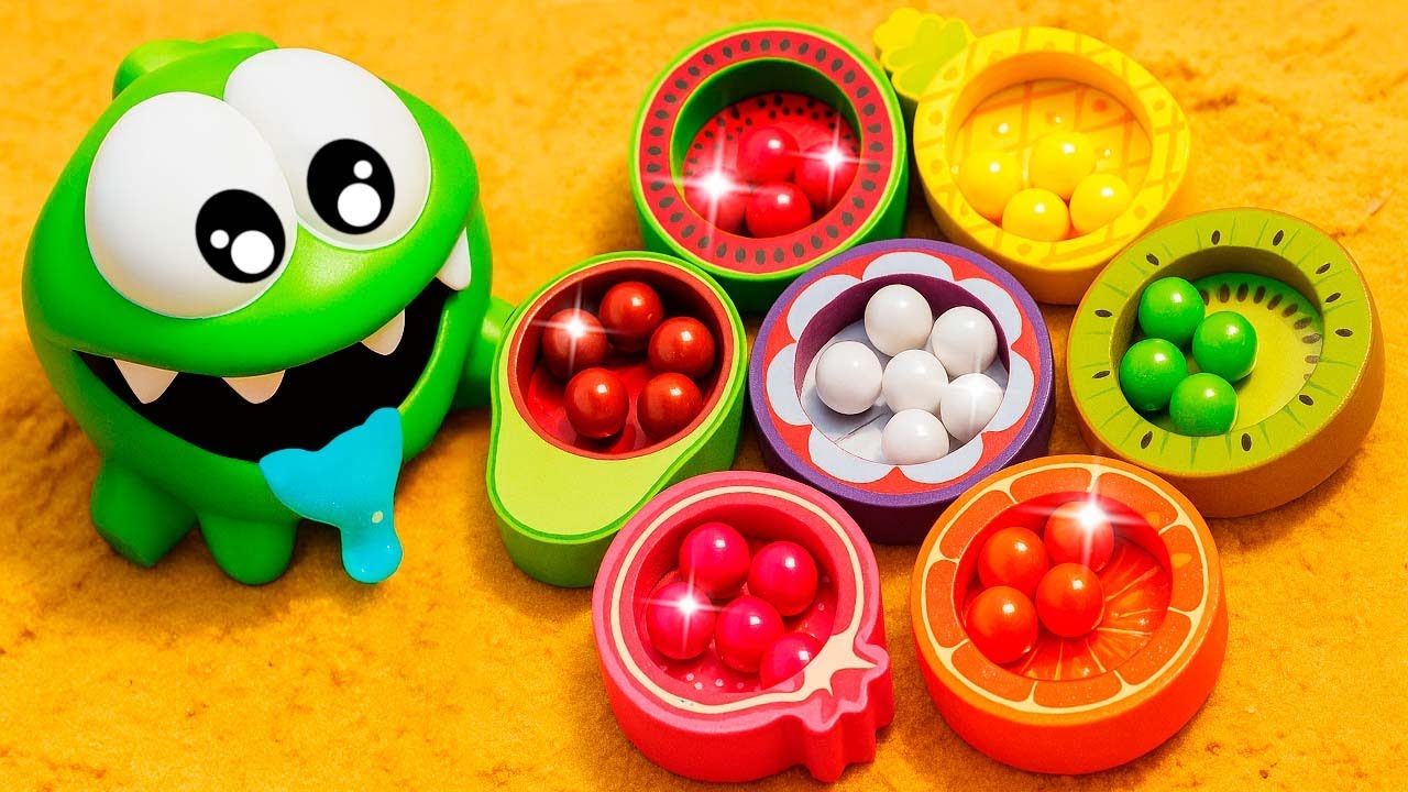 Om Nom juega con frutas y busca bolitas de colores en la arena