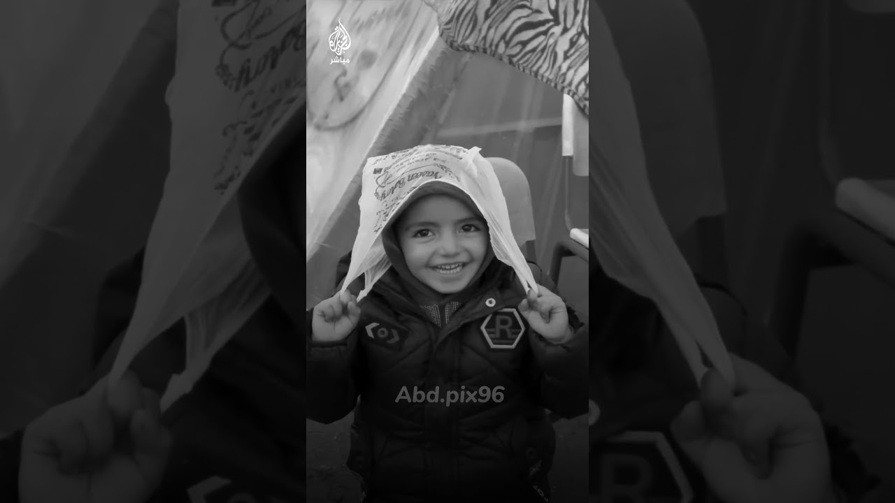 طفل فلسطيني يضع على رأسه كيسًا بلاستيكيًا للاحتماء من المطر في مخيم للنازحين بقطاع غزة