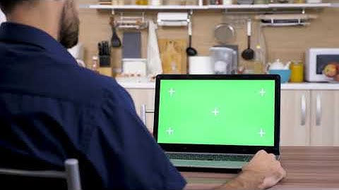 Man in The Kitchen Looking At Computer With Green Screen Mock Up The  has marks