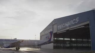 The aircraft enters a hangar. Airplane in hangar with men in background. Passenger aircraft in the