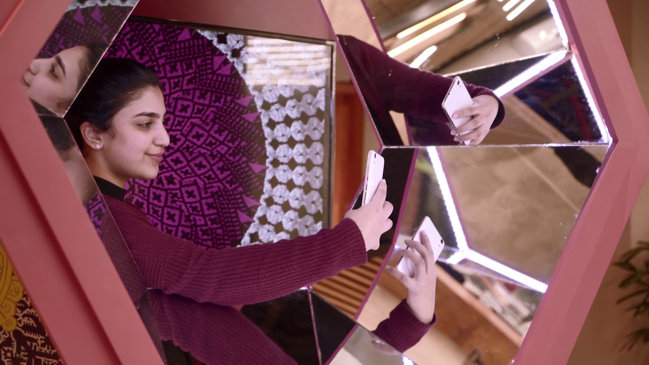 A visitor taking a selfie inside the pink mirrored My Symphony installation