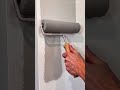 applying grey paint to a vertical wall surface using a paint roller for an even and smooth coverage