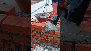 building a red brick wall by applying wet cement mortar with a trowel and aligning with white guidin