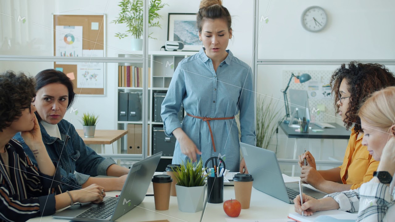 Angry Asian woman yelling at multi-ethnic group of employees talking and gesturing at work