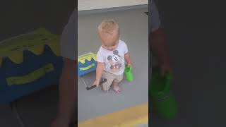 Boy holding green water bottle pulls his wheeled luggage then falls and faceplants on pavement
