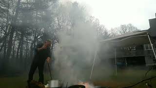 Guy fries a turkey in oversized steel pot in backyard with white canopy