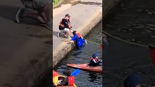 Kid in canal near kayak attempts to get out of water and eventually gets help from an adult