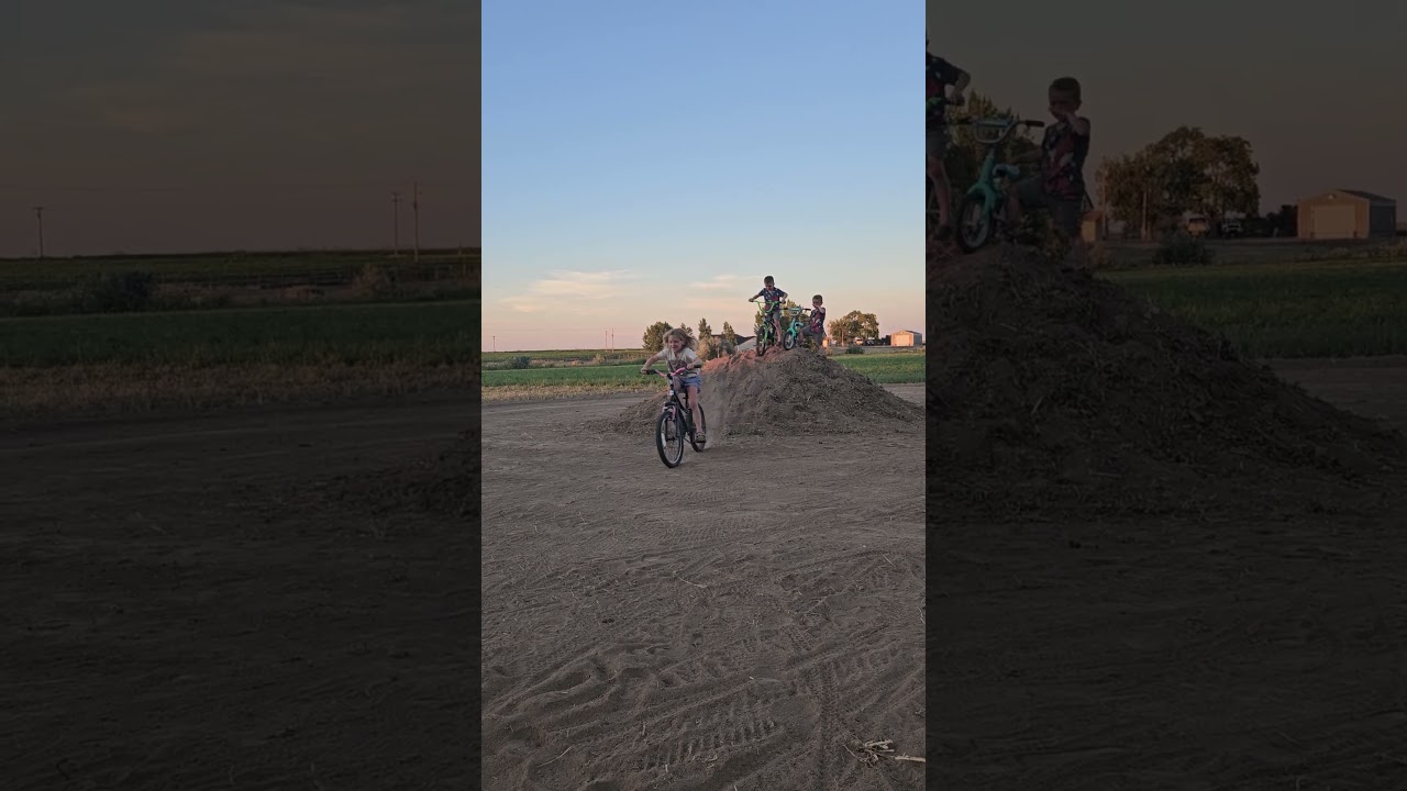 Kids ride bikes down dirt hill then boy falls forward and faceplants then tire hits back of head