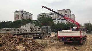 The crane moves the heavy concrete blocks on the truck to the ground in the construction site