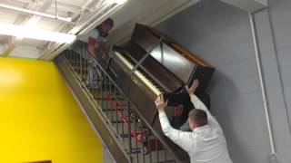 Three guys moving a piano up a flight of stairs