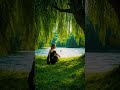 A woman sits by the lakeside under a large tree, quietly enjoying the peaceful view of the water.