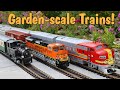 A Steam Train and Two Diesel Model Trains Running Outdoors On A Huge Outdoor Model Train Layout